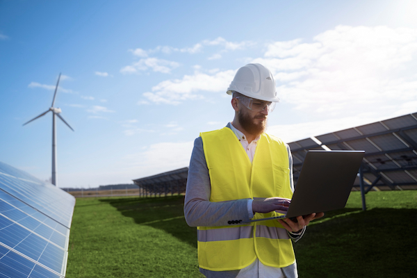 Engineer in safety gear inspecting solar panels with a laptop, representing modern solar industry