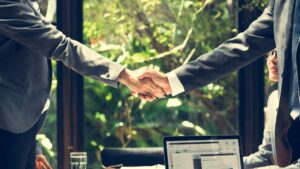 Two business professionals shaking hands after a successful meeting, supported by digital tools for operational efficiency to streamline collaboration