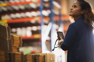 Warehouse worker using a handheld device to track stock, supported by equipment rental business software for inventory management
