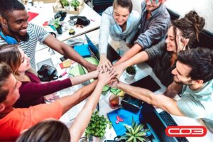 Diverse team collaborating and stacking hands in unity at the office, symbolizing teamwork, service success, and collaboration powered by CO3 Software