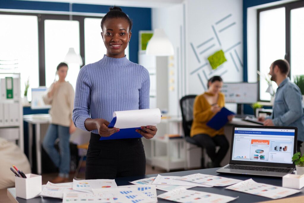 Office professional reviewing documents while a team collaborates in the background, illustrating the need for job tracking software to streamline workflows.
